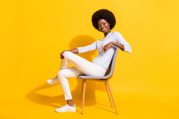 Fototapeta na wymiar Full body profile portrait of adorable dark skin girl sit toothy smile look camera isolated on yellow color background