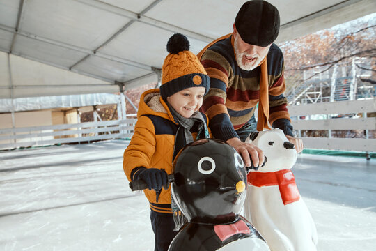 Grandfather and grandson on the ice rink, ice skating, using ice bear figure as prop