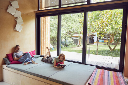 Man using digital tablet and woman reading book while relaxing on bed at home