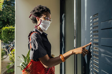 Young woman wearing textile protective mask bringing groceries to a friend