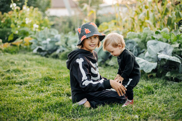 A happy blond boy and his sister in carnival skeleton costumes are playing in the garden on Halloween eve