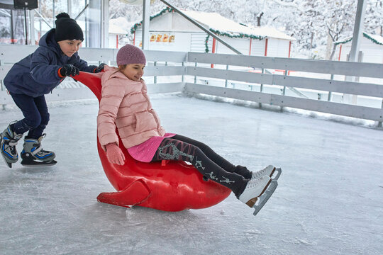 Brother pushing sister on the ice rink,sitting on seal sledge