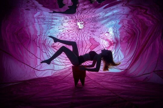 Young woman posing underwater in front of backlit and parachute