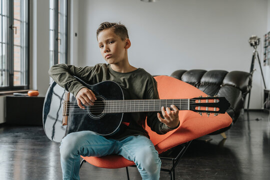 Boy playing guitar while sitting on chair at home