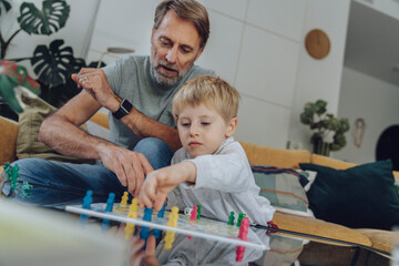 Mature man playing board game with son while sitting in living room