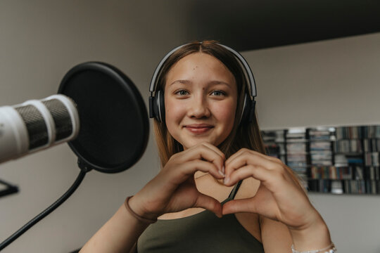 Close-up of smiling teenage girl making heart shape while singing in recording studio