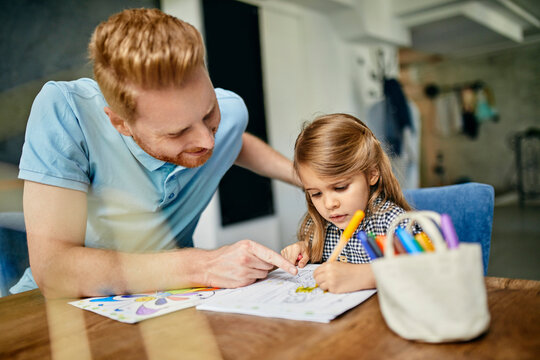 Father and daughter sitting at table, painting colouring book