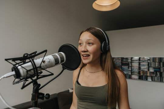 Teenage girl singing over microphone while standing against wall in recording studio