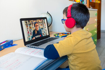 Boy listening to teacher through headphones during video call at home