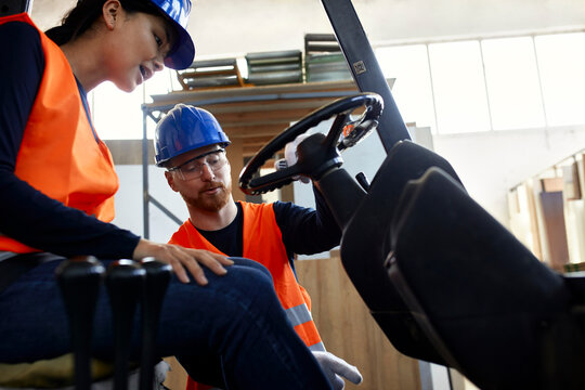 Man instructing female worker on forklift in factory