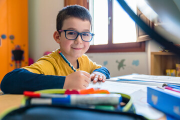 Smiling male student sitting with books at desk during coronavirus