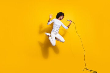 Full body photo of brown haired trendy dark skin lady jump up sing mic isolated on yellow color...