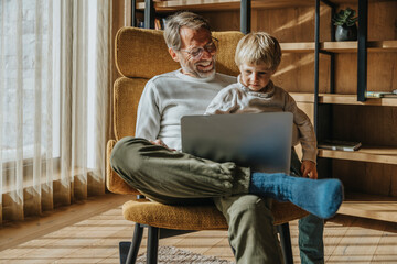 Boy looking at laptop while sitting with father on chair