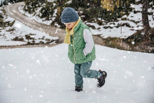 Boy in warm clothing playing in snow while snowing during winter