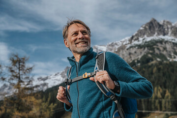 Smiling mature man holding backpack while looking away against sky at Hochkonig, Salzburger Land, Austria