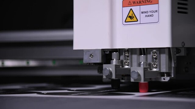 An industrial advertising plotter close-up cuts a template on the cardboard packaging for products. shallow depth of field in real time. Live camera