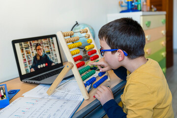 Boy with abacus at desk while teacher on video call during pandemic homeschooling