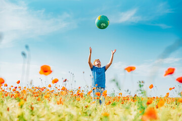 Boy catching globe while standing in poppy field against blue sky on sunny day