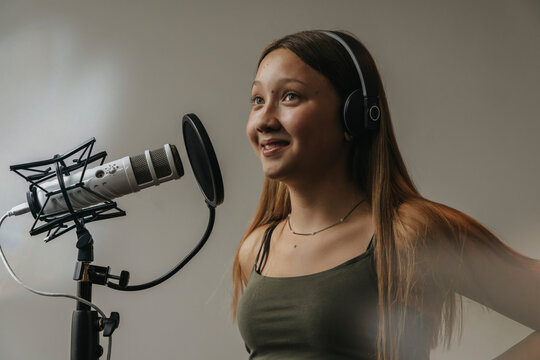 Close-up of smiling teenage girl singing over microphone against wall in recording studio