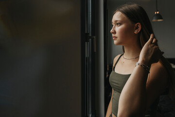 Thoughtful teenage girl looking through window while standing at home