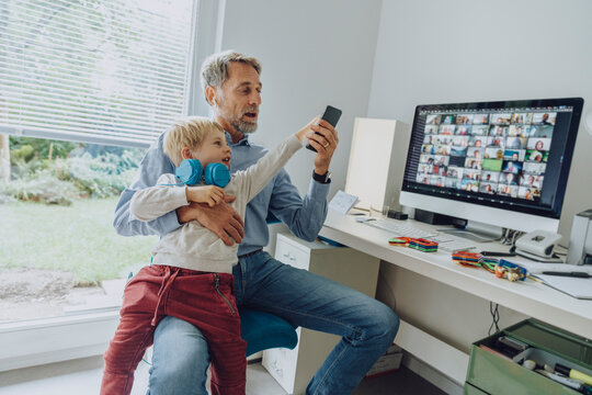 Son distracting father through smart phone while video conferencing at home office