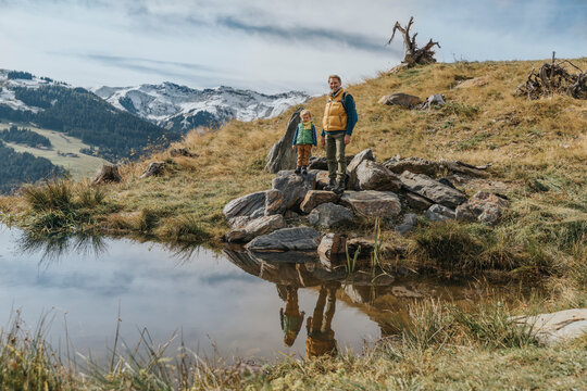 Mature man with son standing on rock by pond against sky at Salzburger Land, Leogang Mountains, Austria