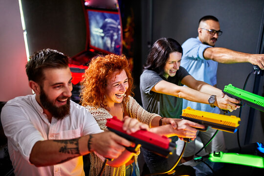 Happy friends playing and shooting with pistols in an amusement arcade