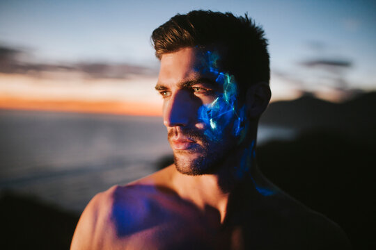 Thoughtful young man with ultraviolet paint on face