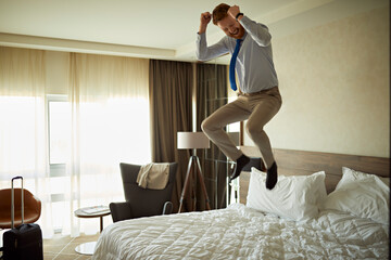Excited businessman jumping on bed in hotel room