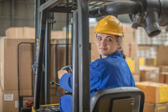 Smiling woman wearing hard hat driving forklift in factory