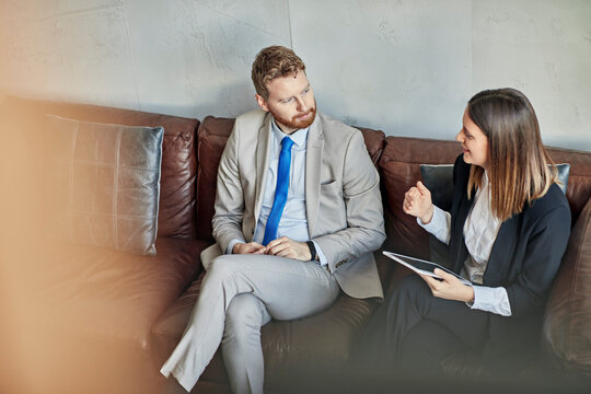 Businessman and businesswoman with tablet sitting on couch in hotel lobby