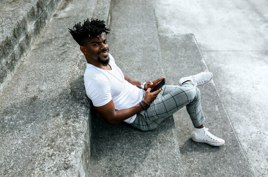 Smiling African man using smart phone while sitting on steps