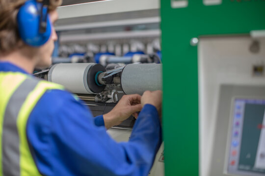 Man wearing ear defenders working at spool machine in factory
