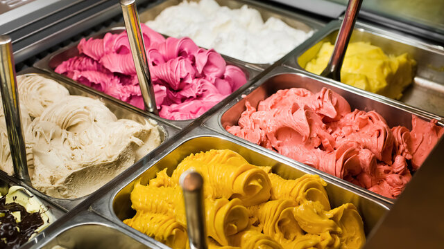 Multi colored Italian ice cream gelato with various fruit flavors decorated with fruits, nuts or chocolate  in the refrigerator-display case. Ice cream trays.
Italian cuisine. Gourmet dessert.
