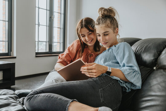 Friends using digital tablet while relaxing on sofa at home