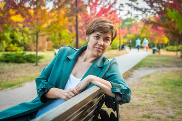 middle-aged woman sits on a bench in the autumn park. orange leaves. concepts about senior people