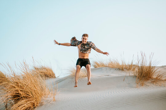 Young man with unbuttoned shit jumping on sand at Almeria, Tabernas desert, Spain
