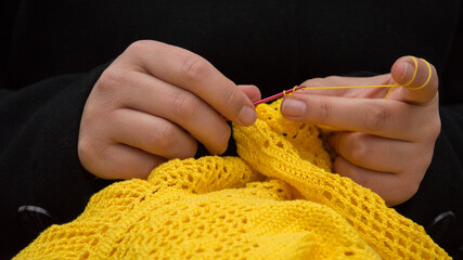 The hands of a woman crocheting a yellow jumper.