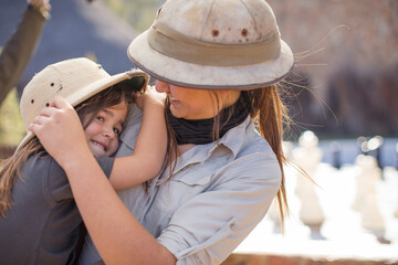 Happy girl embracing young woman wearing pith helmet