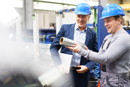 Businessman and worker in a factory holding steel pipe
