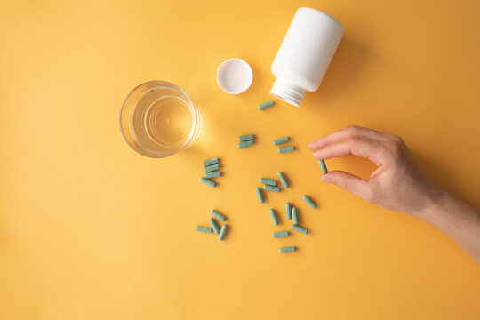 Studio shot of glass of water and hand of woman taking nutritional supplement capsules - Powered by Adobe