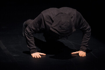 Dancer wearing black hood crouching on stage