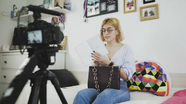 A young woman with glasses smiles and tells the camera about a new purchase. Unboxing