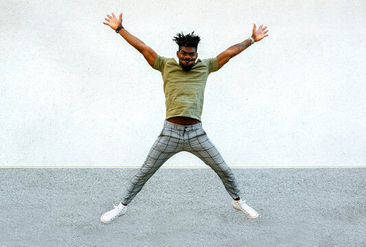 Carefree mid adult man with arms raised jumping against wall in city