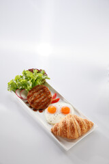 Grilled hamburger, Puffy croissant and Fried egg on long plate isolated on white background.