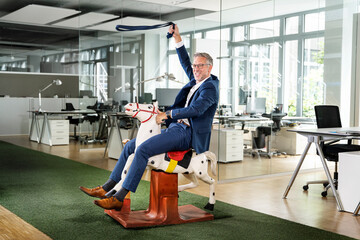 Playful male professional pretending to ride rocking horse at office