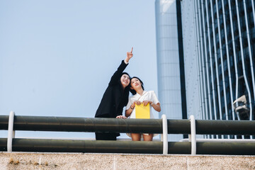 Smiling businesswoman pointing female coworker at downtown district in city against clear sky