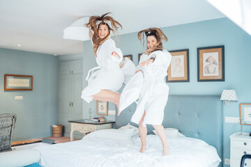 Cheerful twin sisters jumping on bed in hotel room