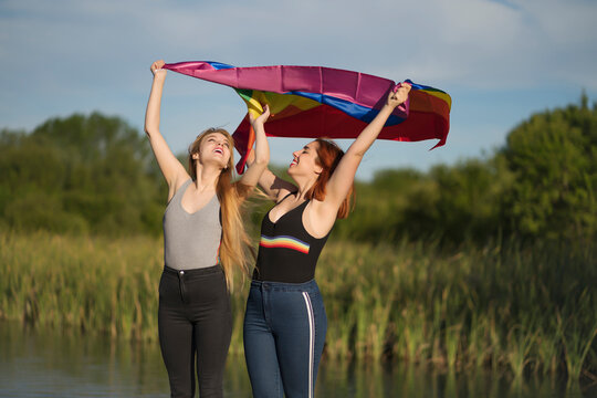 Cheerful lesbian couple holding multi colored flag while standing sky