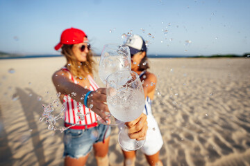 Mid adult female friends splashing drink while toasting at beach on sunny day